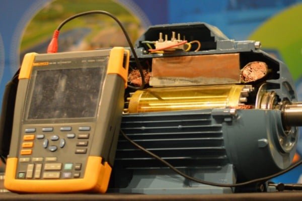 Maintenance technician using a specialized probe and oscilloscope to measure shaft voltage levels on a running motor.