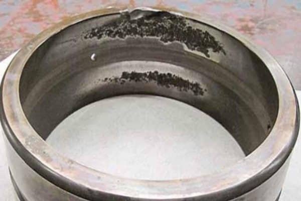 A bearing race displaying large, irregular spots where metal has flaked away, revealing sharp, fractured edges.